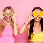 OMG! Verbaasd verbaasde zich verbaasd aantrekkelijk vrij gelukkig lachend charmante vrolijke funky vrouwen zijn gek rond en bedekken hun ogen met sap kiwi en sinaasappel, geïsoleerd op fel roze achtergrond