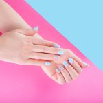 Vrouwelijke handen met een zacht blauwe kleur gel lac of gelnagellak op haar vingernagels geïsoleerd op een roze en blauwe achtergrond