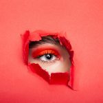 Kalm vrouwelijk model met rode minerale oogschaduw van minerale make-up van bellapierre die wegkijkt door gescheurd rood papier in studio