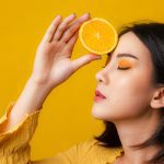 Mode minerale make-up van bellapierre cosmetische oranje concept. Aziatische vrouw met oranje fruit op banner gele achtergrond.