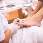 Een voetverzorgster die de voet van een vrouw behandeld tijdens de opleiding pedicure - basis van Blue Sage