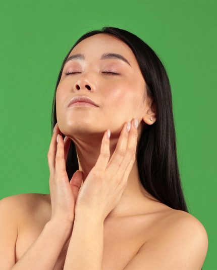 mooie jonge aziatische vrouw die de dag en nacht crème gebruikt van 24nexx, geïsoleerd op een groene achtergrond
