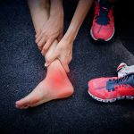 Vrouwelijke runner voet aan te raken met pijn als gevolg van verstuikte enkel in park. Gebroken verdraaide enkel, blessure door inspanning. Acute pijnprikkel