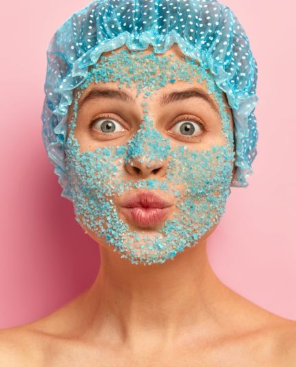 Headshot van mooie vrouw met ronde lippen, draagt ​​witte douchemuts, peeled gezicht met organische natuurlijke mint ice peeling, gezichtsscrub, lichaamsscrub, kijkt recht naar camera, wacht op effectief resultaat van schoonheidsproduct, huid verbeterende producten Blue Sage Shop