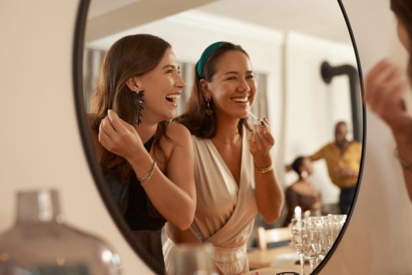 twee jonge vrouwen die naar een spiegel kijken en zich maquilleren tijden de workshop avond make-up bij Blue Sage