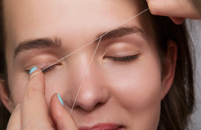close up van een vrouw haar gezicht waarbij threading ontharing van de wenkbrauwen wordt uitgevoerd door een Blue Sage specialiste